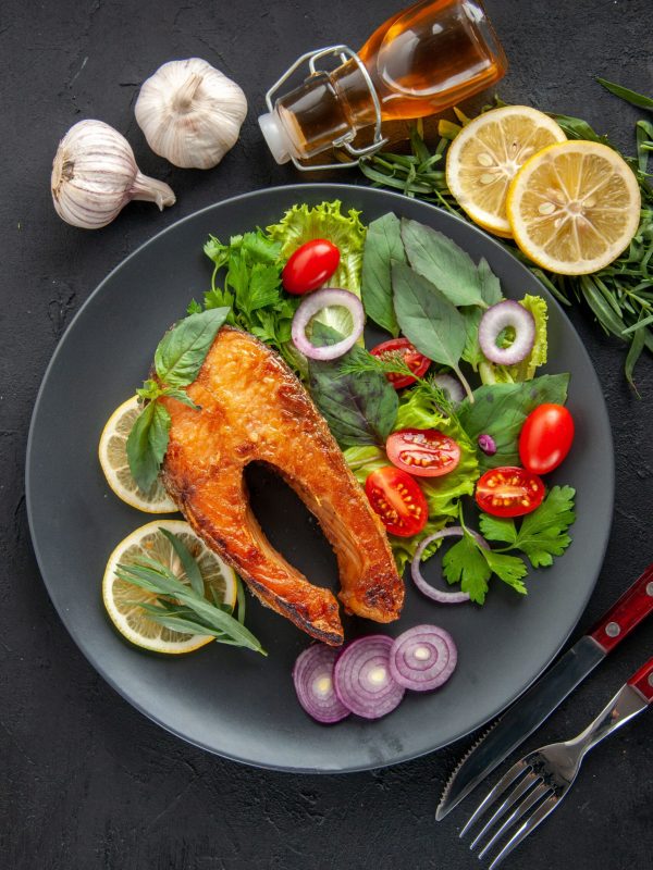 top-view-tasty-cooked-fish-with-fresh-vegetables-seasonings-dark-table-min